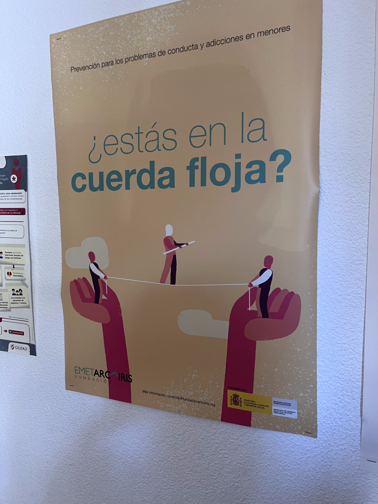 Plakat hiszpańskiej fundacji EMET Arco Iris dotyczący profilaktyki uzależnień u nieletnich. Zawiera pytanie „¿estás en la cuerda floja?” (czy jesteś na linie?) oraz ilustrację linoskoczka asekurowanego przez dłonie.